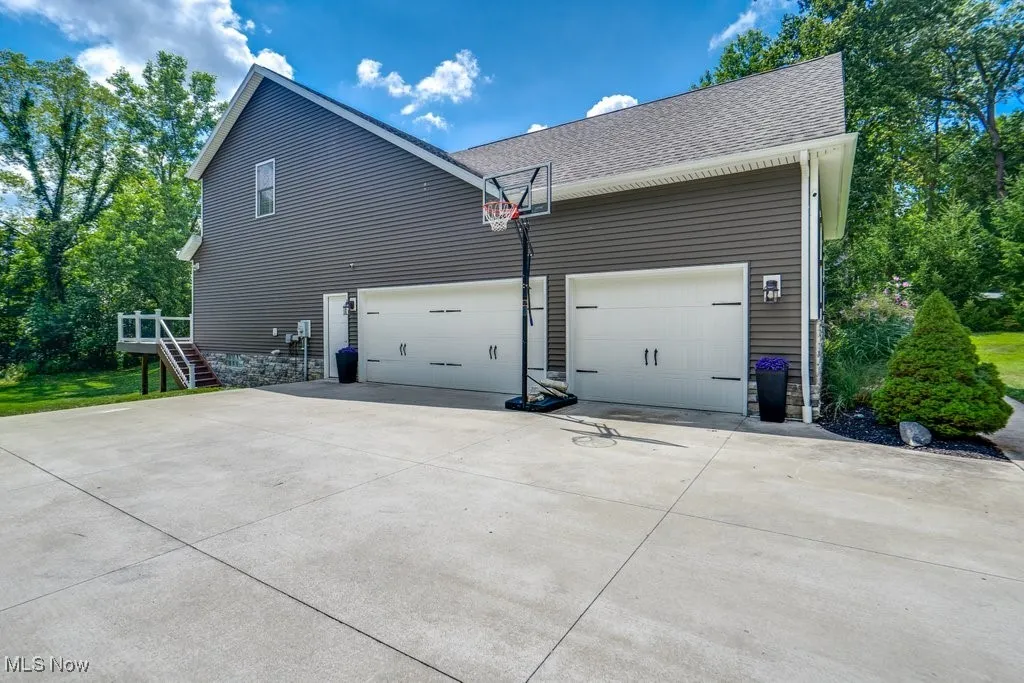 View of side of home with concrete driveway, stairs, an attached garage, and a shingled roof