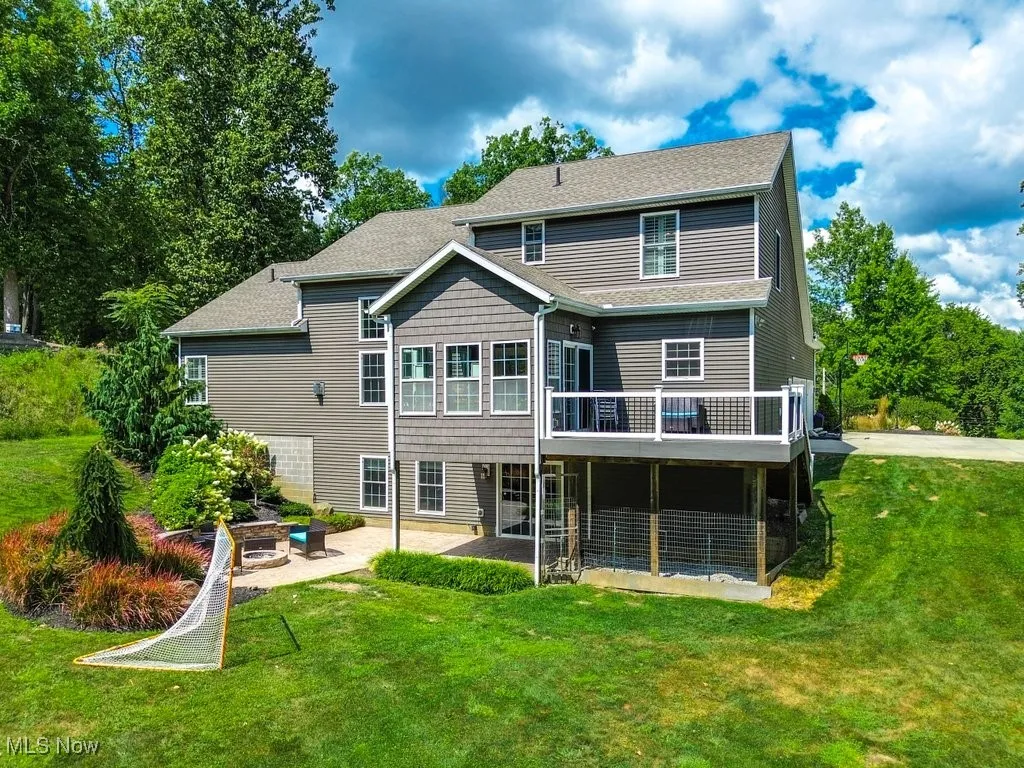 Back of house featuring a lawn, a patio, roof with shingles, and a wooden deck