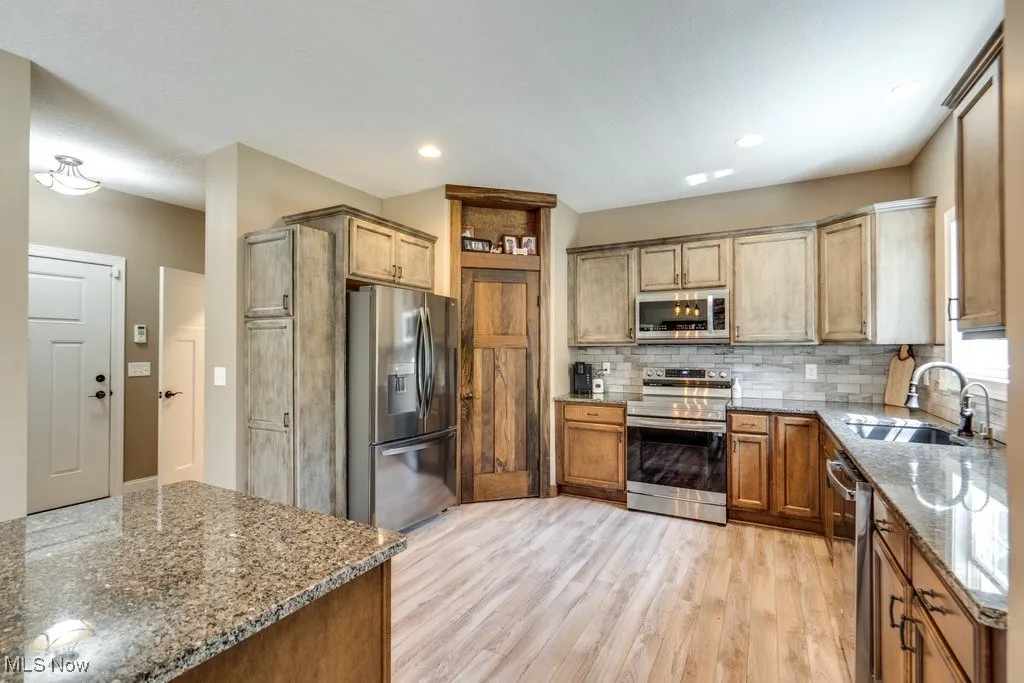 Kitchen featuring light stone countertops, appliances with stainless steel finishes, backsplash, light wood-style flooring, and recessed lighting