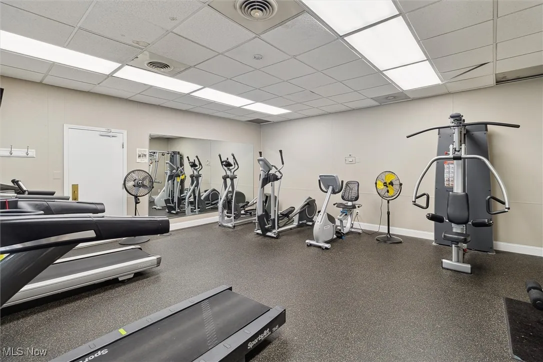 Gym with a paneled ceiling and baseboards