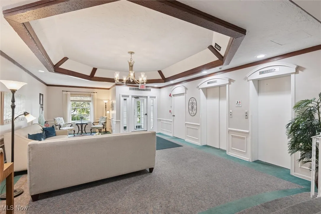 Lobby area with a tray ceiling, ornamental molding, carpet floors, elevator, and a decorative wall