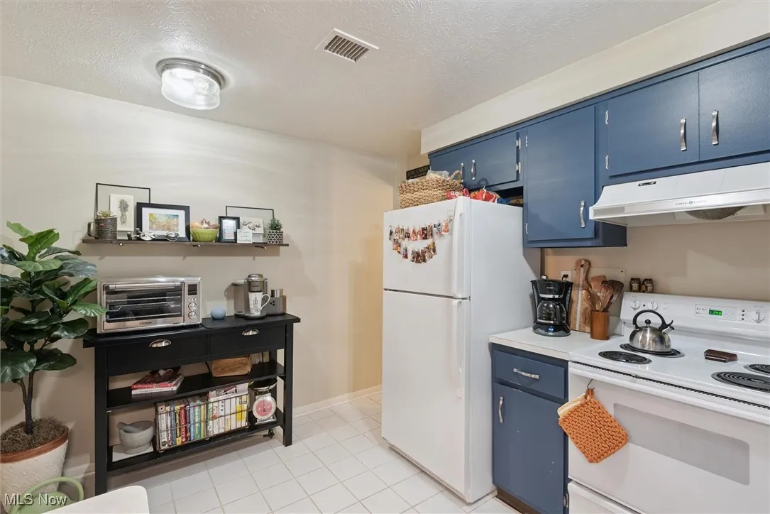 Kitchen featuring blue cabinetry, white appliances, light countertops, a textured ceiling, and under cabinet range hood