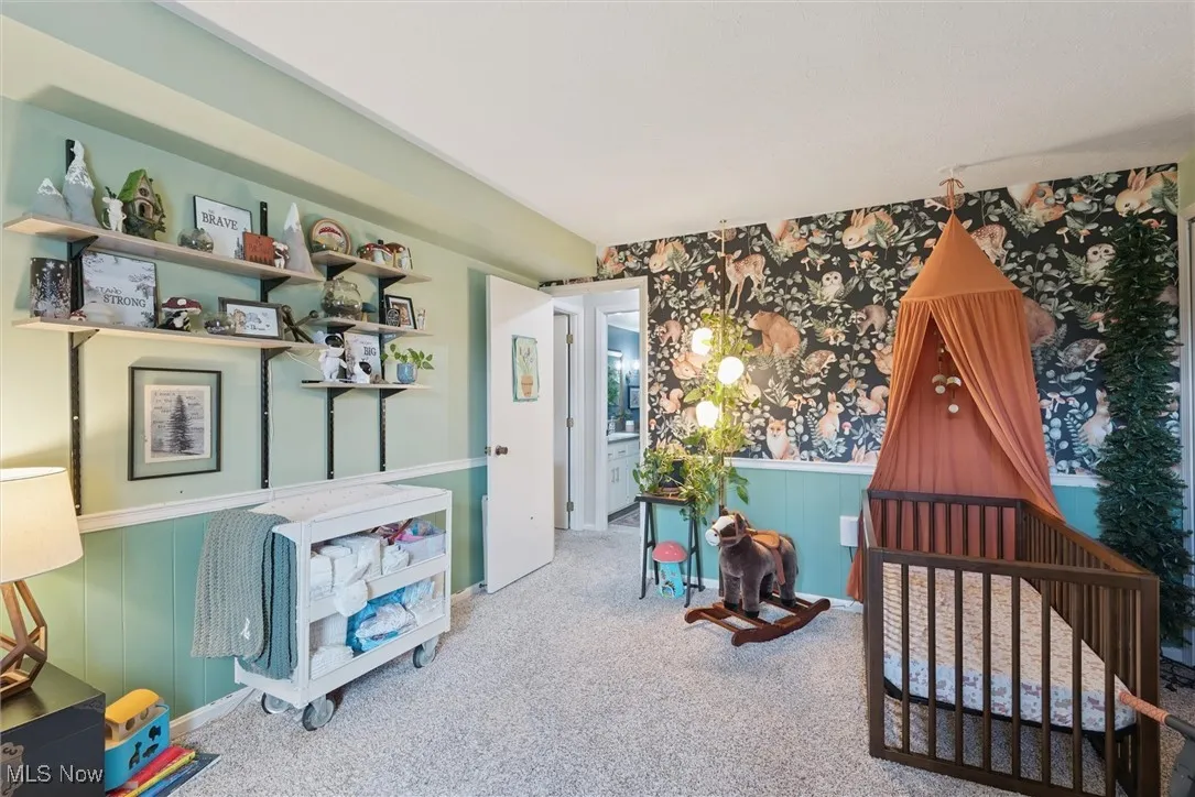 Carpeted bedroom with wainscoting, wallpapered walls, a crib, and wood walls