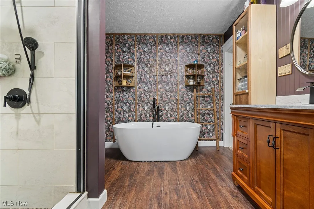 Bathroom with a freestanding bath, a textured ceiling, dark wood-type flooring, vanity, and a stall shower