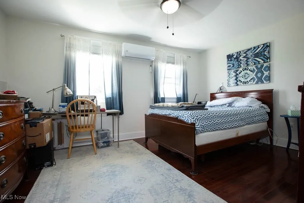 Bedroom featuring wood finished floors, ceiling fan, a wall unit AC, and a desk