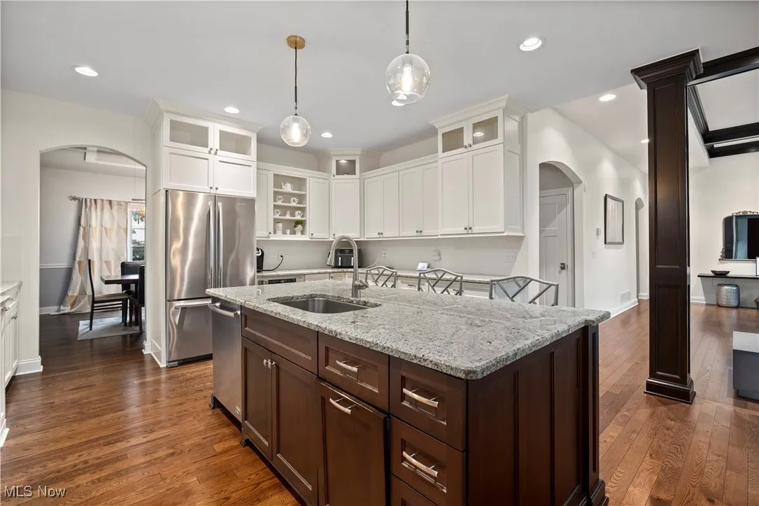 Kitchen with arched walkways, dark brown cabinetry, light stone countertops, dark wood-type flooring, and recessed lighting