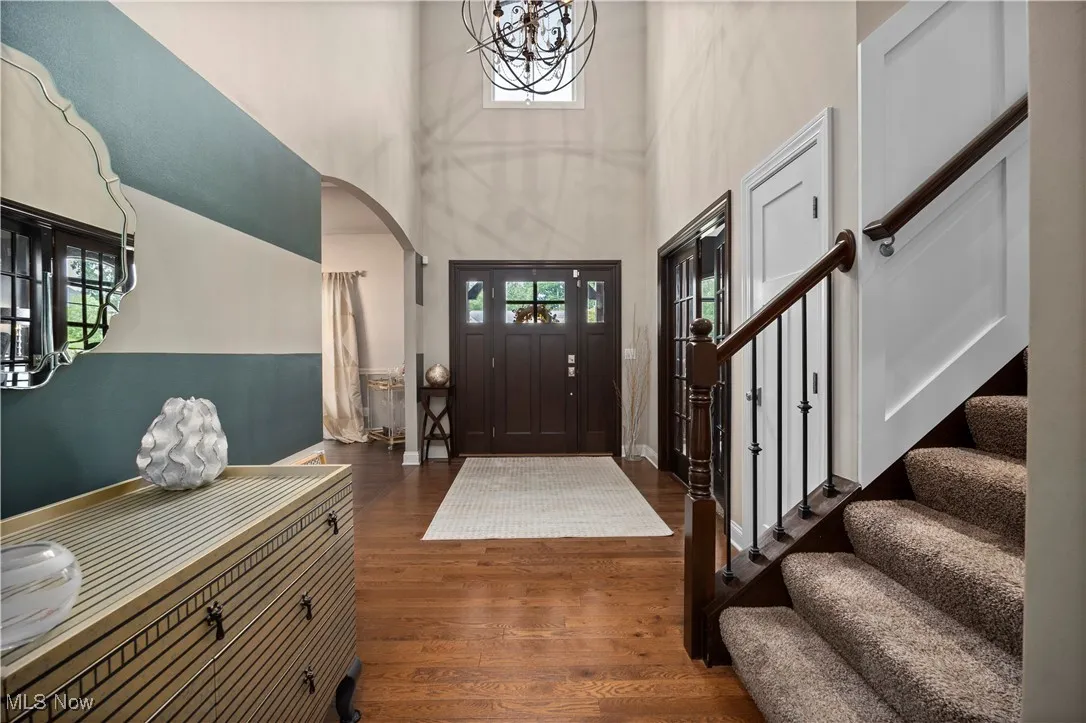 Foyer with dark wood-style floors, a high ceiling, stairway, arched walkways, and a chandelier