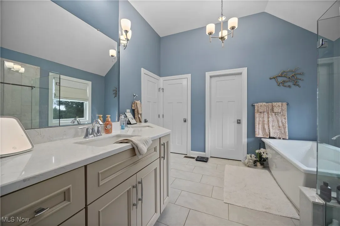 Bathroom featuring vanity, a freestanding bath, a stall shower, a chandelier, and light tile patterned floors