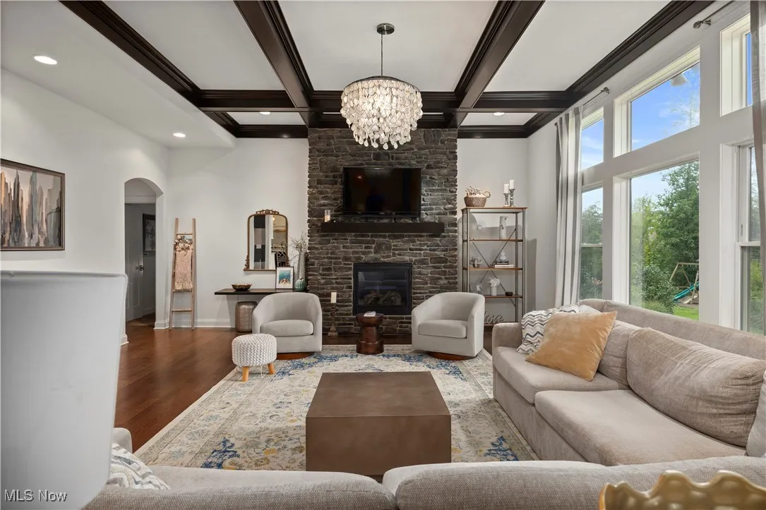 Living room with a fireplace, wood finished floors, arched walkways, beamed ceiling, and coffered ceiling