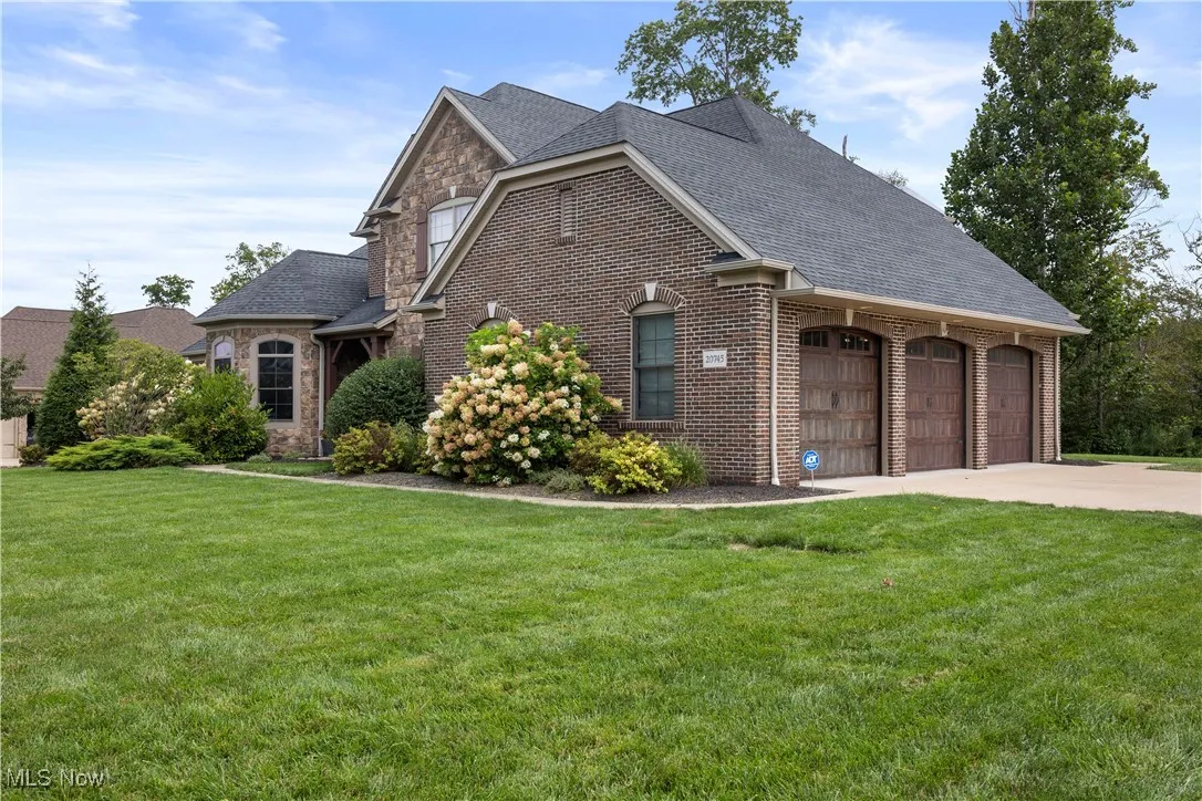 View of front facade featuring a shingled roof, a front yard, brick siding, and concrete driveway