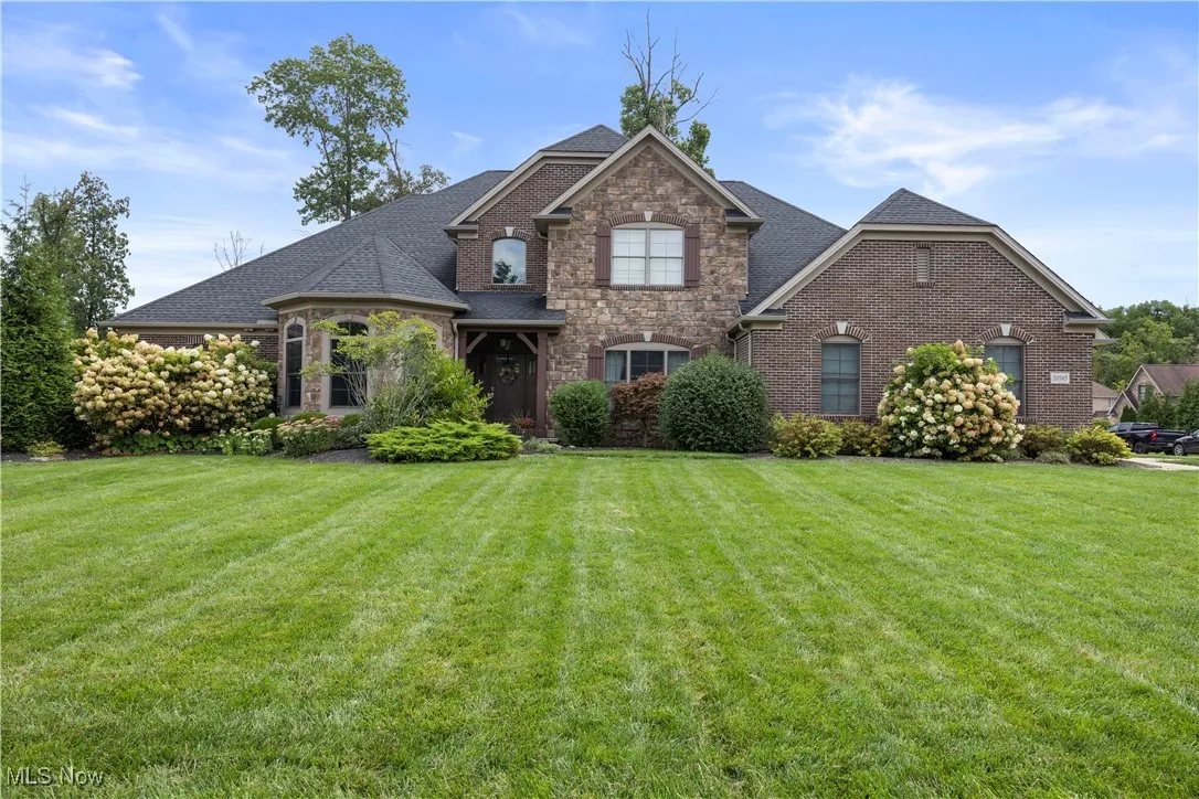 View of front of property with roof with shingles, a front yard, and stone siding