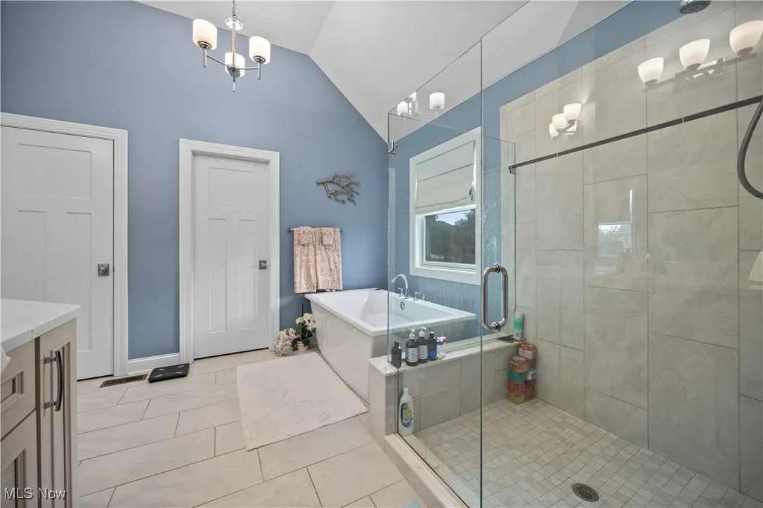 Bathroom featuring a stall shower, a freestanding bath, lofted ceiling, vanity, and a chandelier