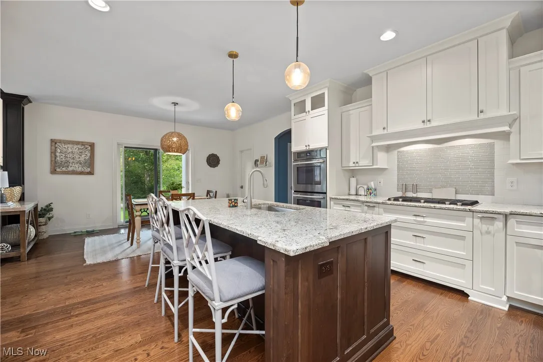 Kitchen with decorative backsplash, dark brown cabinetry, light stone counters, recessed lighting, and a breakfast bar