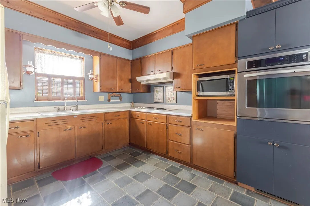 Kitchen with appliances with stainless steel finishes, light countertops, brown cabinets, and under cabinet range hood
