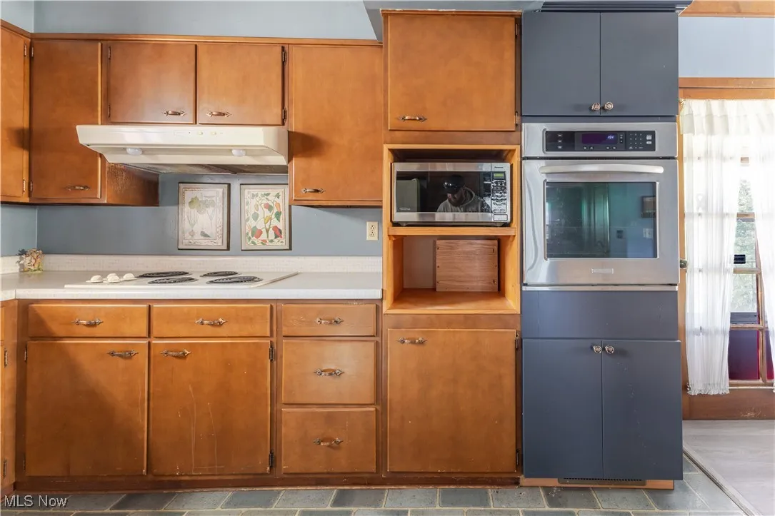 Kitchen featuring stainless steel appliances, under cabinet range hood, brown cabinets, and tile countertops