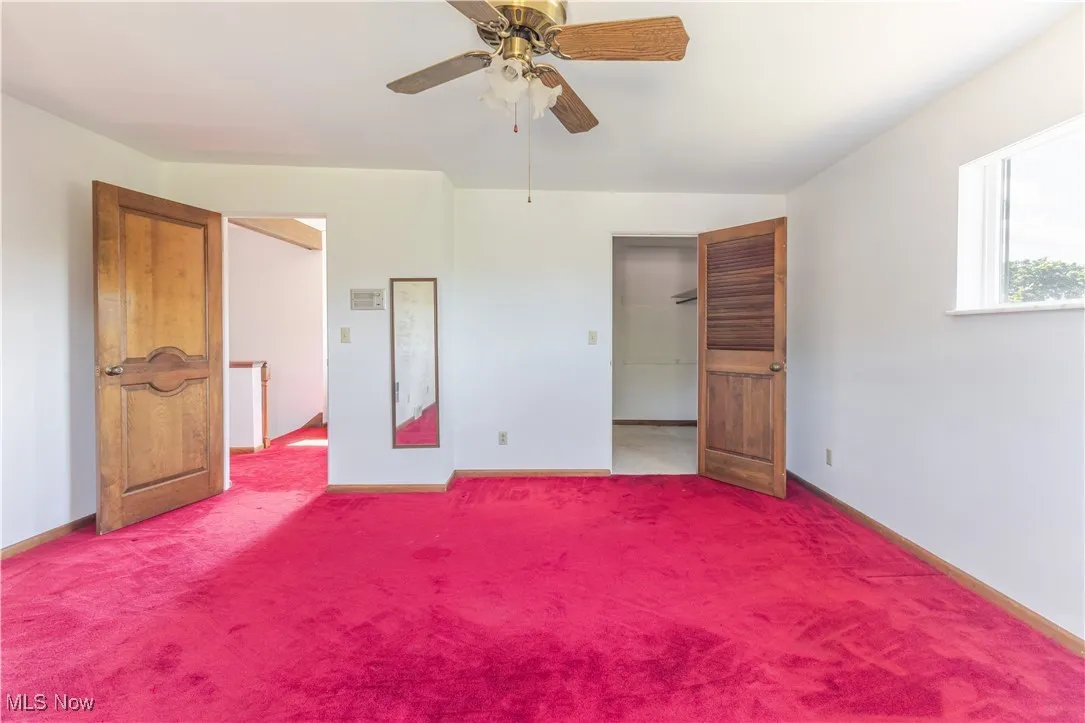 Unfurnished bedroom with carpet, a ceiling fan, and a spacious closet