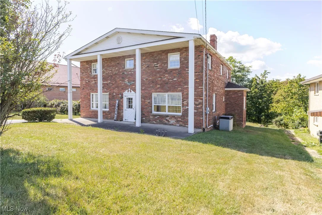 Greek revival house with a front yard, brick siding, a chimney, and a porch
