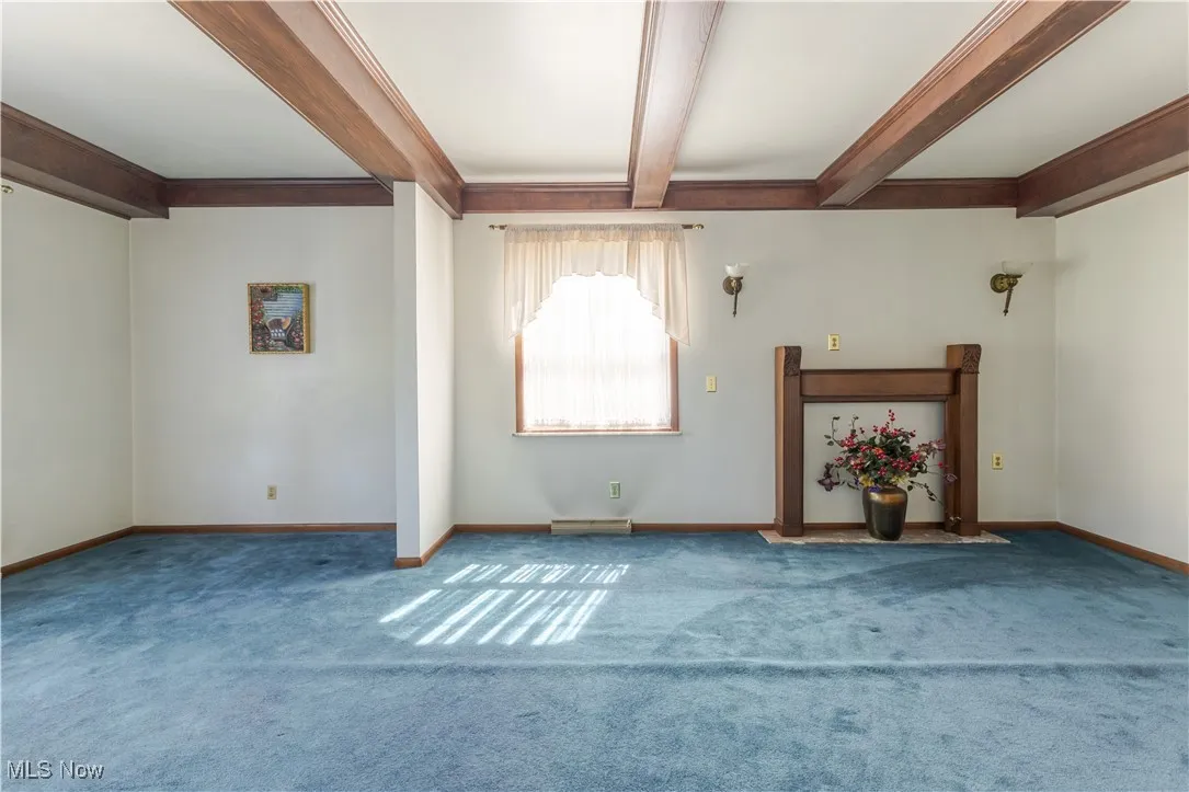 Unfurnished living room featuring beam ceiling and carpet floors
