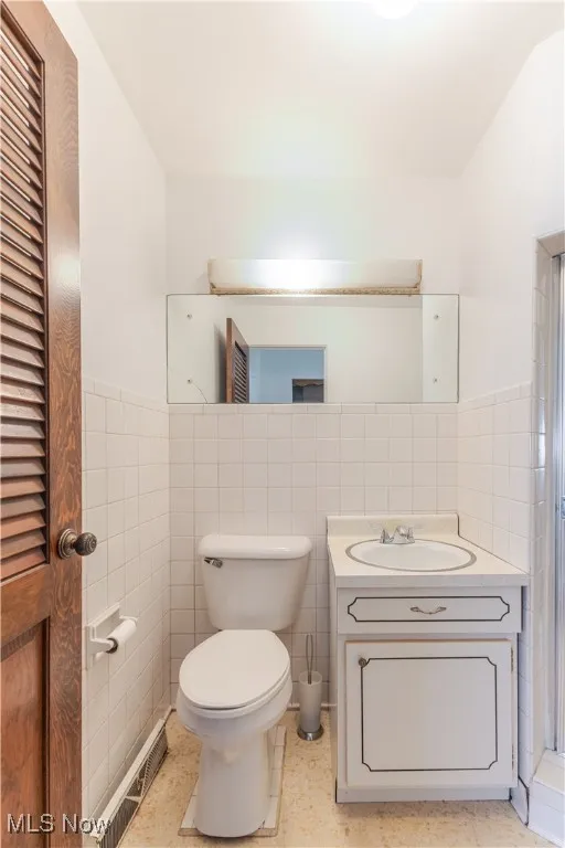 Full bath with tile walls, vanity, a wainscoted wall, a closet, and a shower