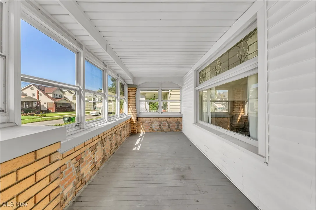 Unfurnished sunroom with a residential view, hardwood / wood-style floors, and brick wall