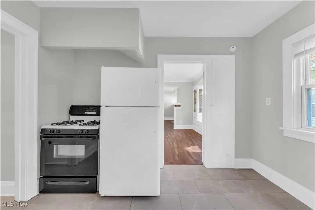Kitchen with freestanding refrigerator, black gas range oven, and light tile patterned flooring