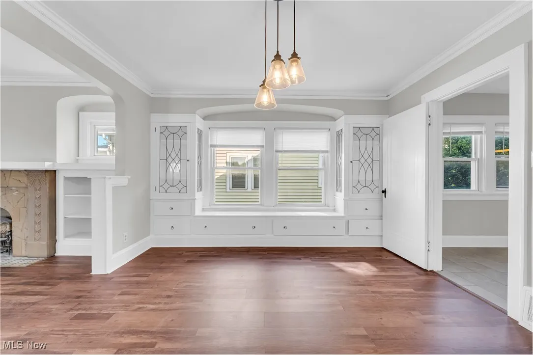 Unfurnished dining area featuring plenty of natural light, crown molding, wood finished floors, and a fireplace with flush hearth