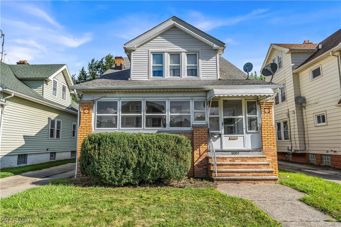 Bungalow-style house featuring a sunroom, roof with shingles, brick siding, and a front lawn