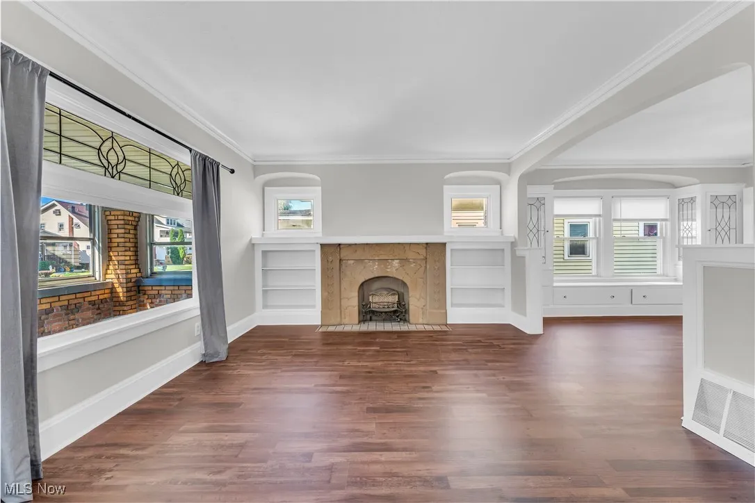 Unfurnished living room with crown molding, dark wood-style flooring, plenty of natural light, and a tiled fireplace