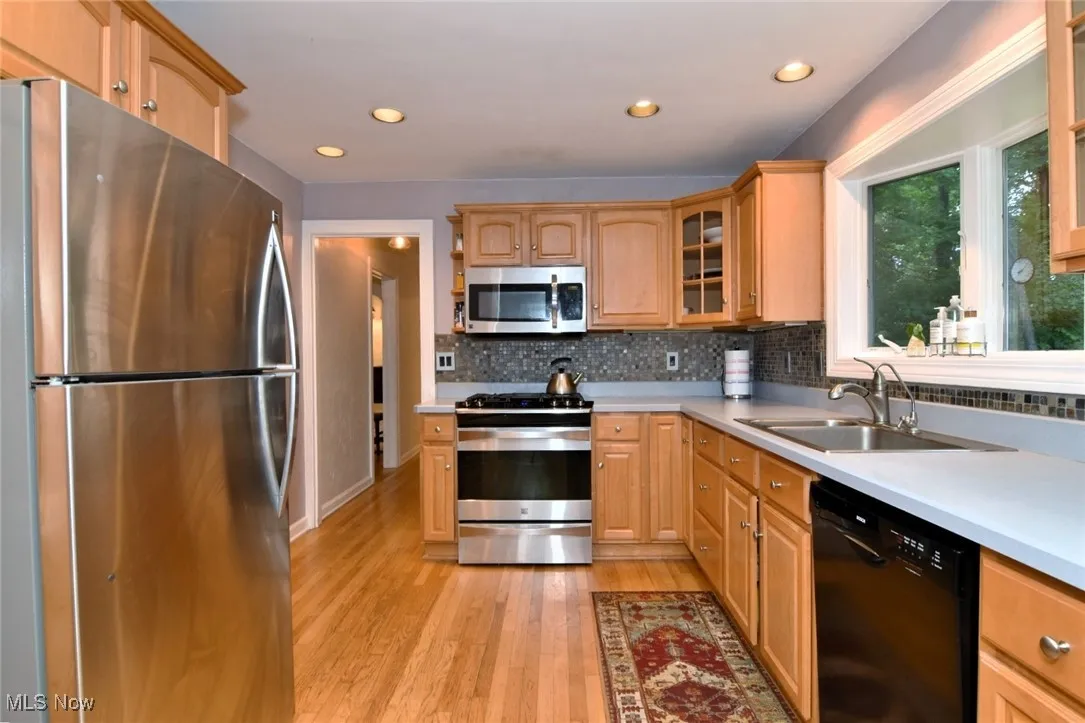 Kitchen featuring appliances with stainless steel finishes, light wood-style flooring, glass insert cabinets, tasteful backsplash, and recessed lighting