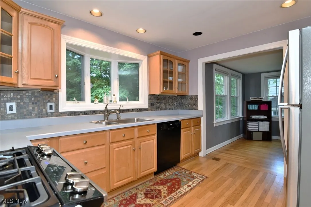 Kitchen featuring glass insert cabinets, freestanding refrigerator, light wood-style floors, black dishwasher, and backsplash
