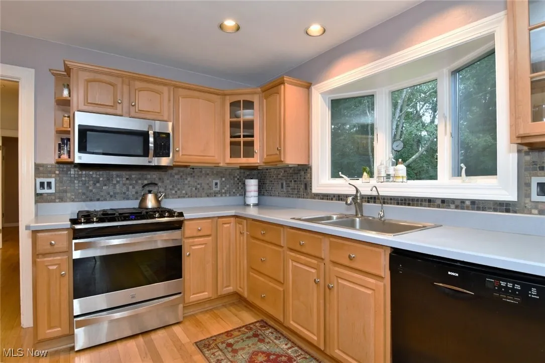 Kitchen featuring glass insert cabinets, stainless steel appliances, backsplash, light countertops, and recessed lighting