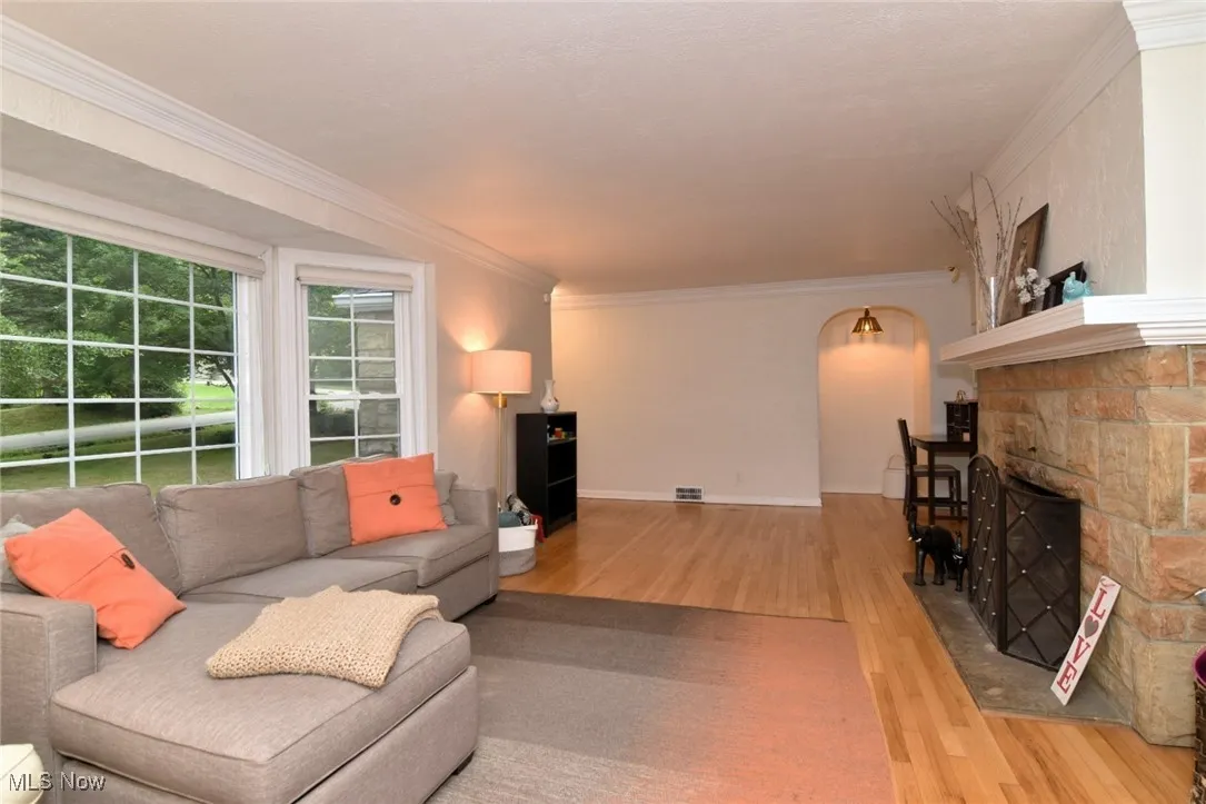 Living area with ornamental molding, wood finished floors, a stone fireplace, and arched walkways