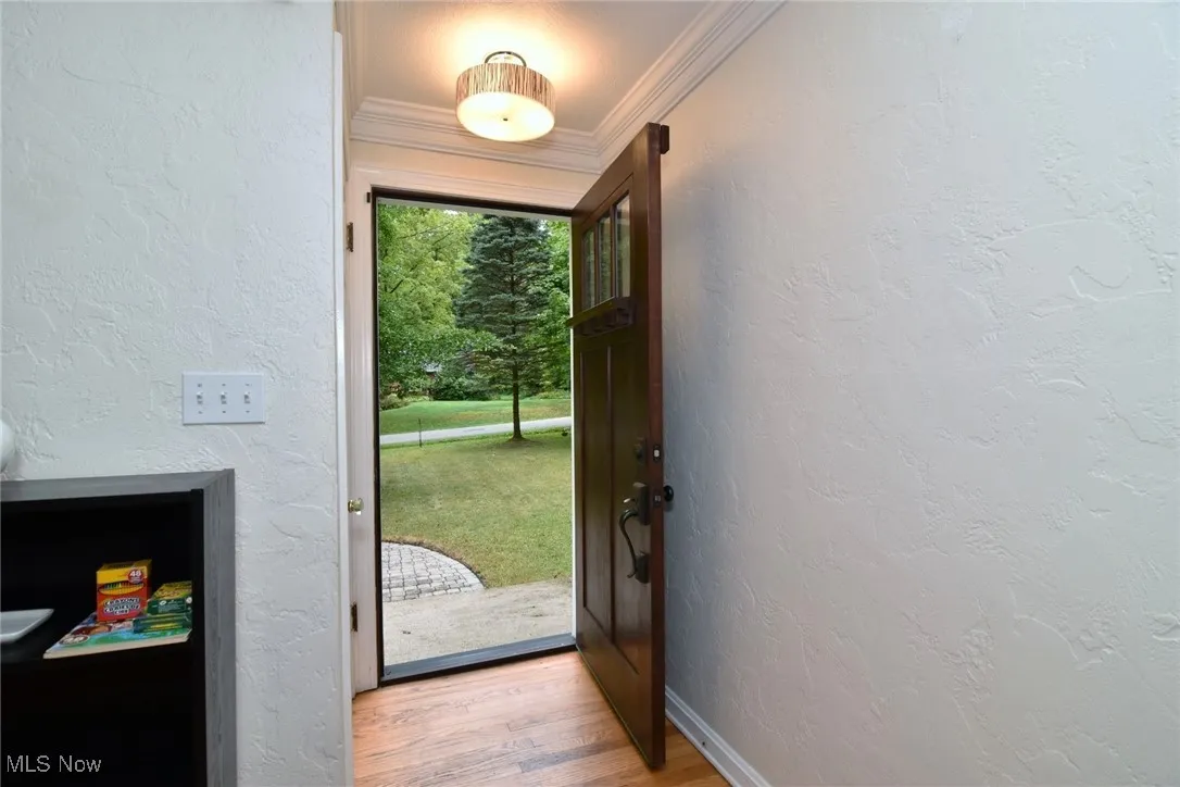 Doorway to outside with a textured wall, wood finished floors, and ornamental molding