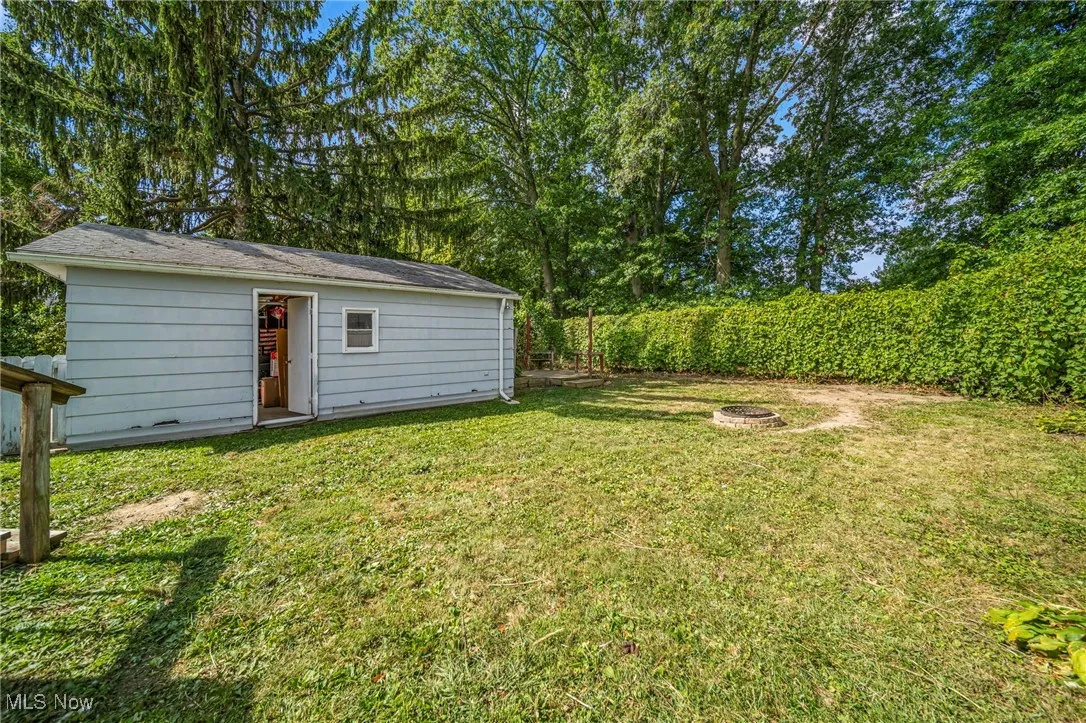 View of grassy yard with an outbuilding, an outdoor fire pit, and view of scattered trees