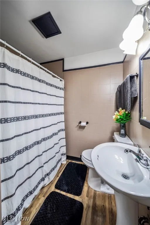 Full bath with tile walls, wood finished floors, and a shower with shower curtain