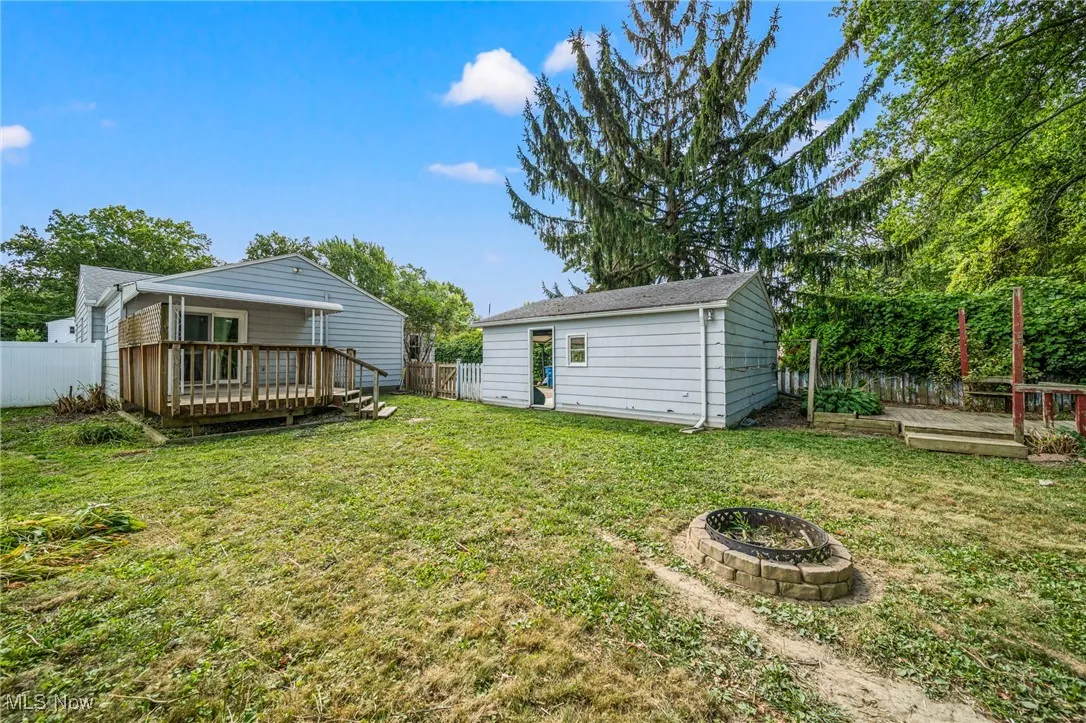 Fenced backyard featuring a deck, an outbuilding, and a fire pit