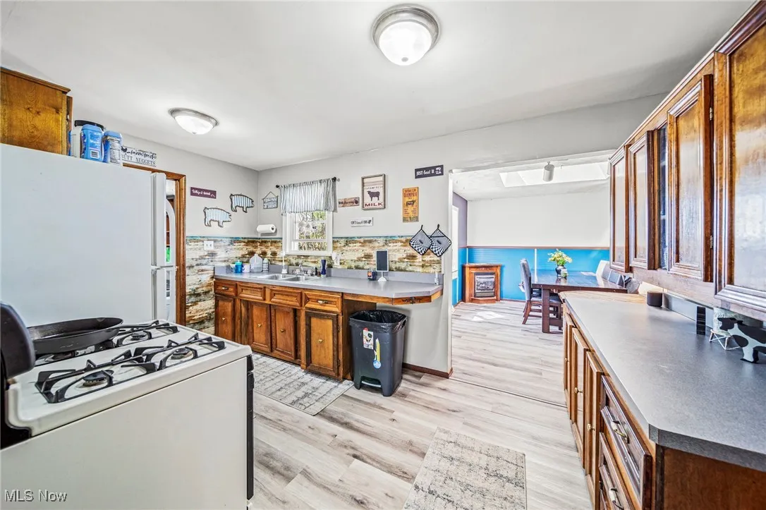 Kitchen featuring white appliances, light wood-style floors, brown cabinetry, light countertops, and a wainscoted wall