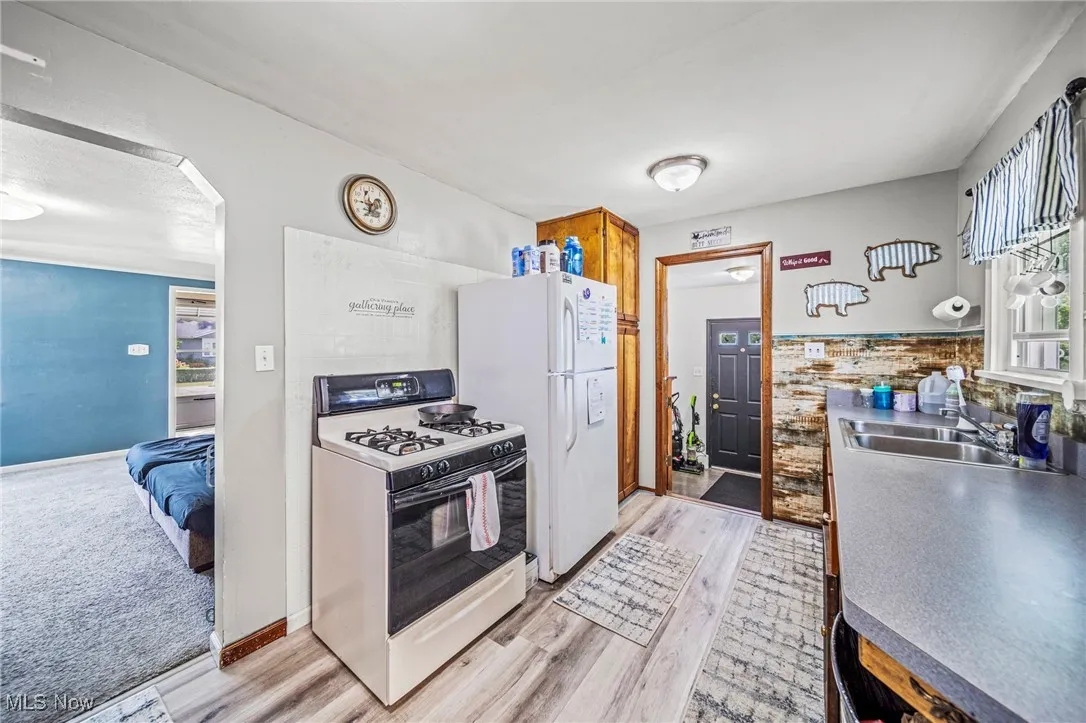 Kitchen featuring white gas stove, light wood-type flooring, arched walkways, and brown cabinetry