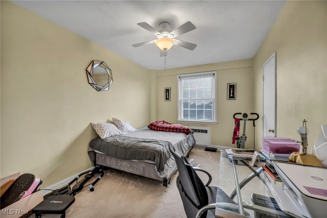 Bedroom featuring light colored carpet, a ceiling fan, and radiator heating unit