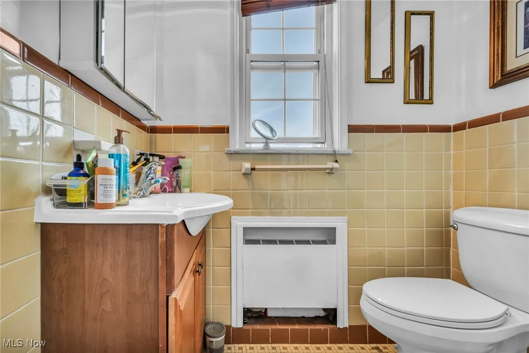 Bathroom featuring vanity, tile walls, radiator, dark tile patterned floors, and wainscoting