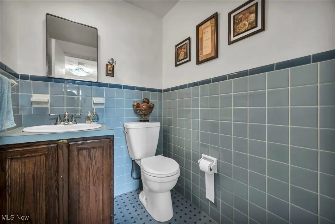 Half bath featuring tile walls, a wainscoted wall, vanity, and tile patterned floors