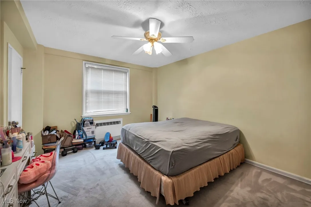 Carpeted bedroom featuring a textured ceiling, ceiling fan, and radiator heating unit