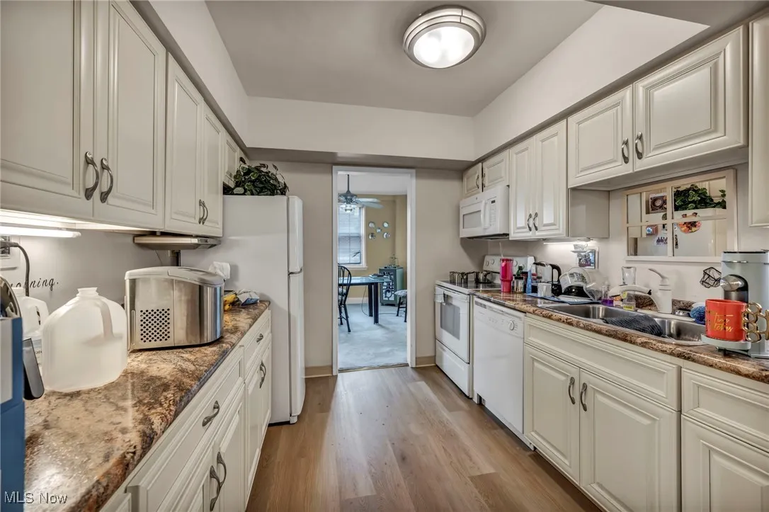 Kitchen featuring light wood-style flooring, white appliances, white cabinets, ceiling fan, and dark stone counters