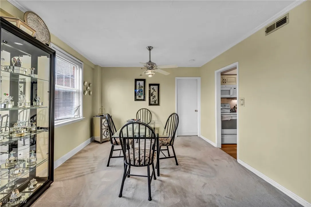 Dining space with ornamental molding, light carpet, and ceiling fan