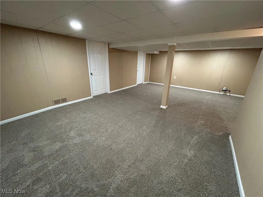 Finished basement featuring dark colored carpet and a paneled ceiling