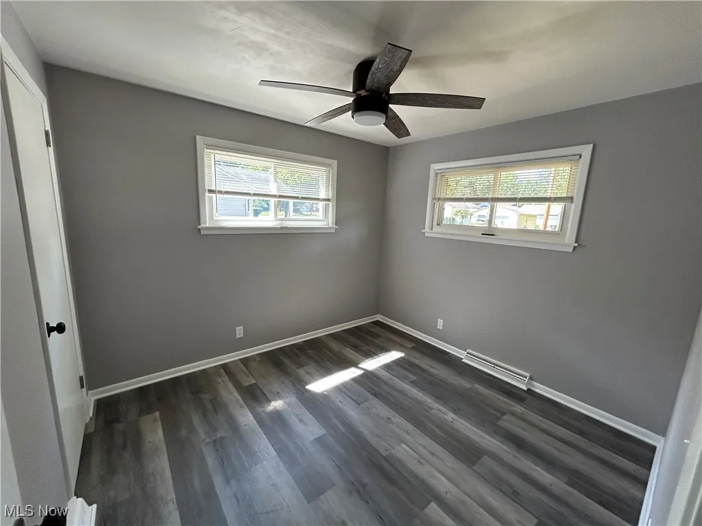 Unfurnished bedroom featuring a closet, multiple windows, dark wood finished floors, and a ceiling fan