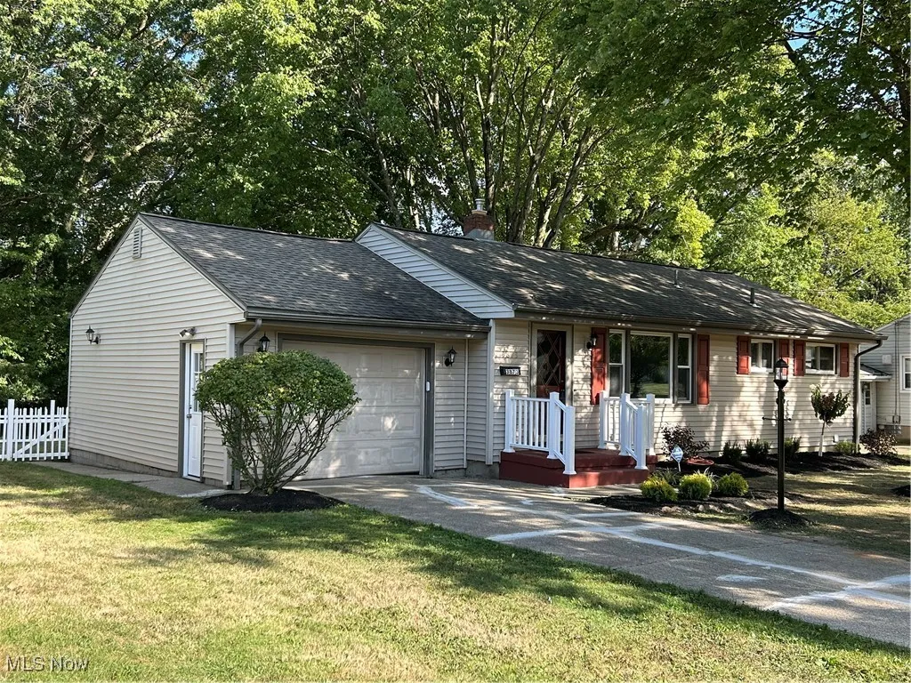 Ranch-style house with roof with shingles, concrete driveway, an attached garage, a chimney, and view of wooded area