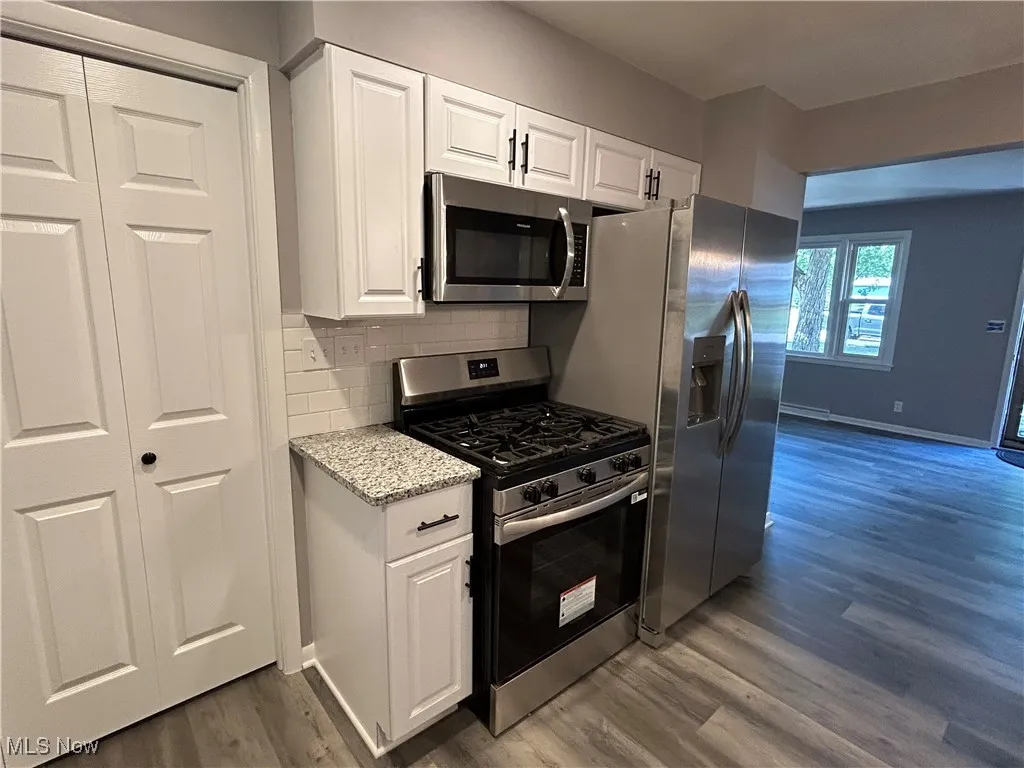 Kitchen featuring stainless steel appliances, white cabinets, dark wood-style floors, and decorative backsplash