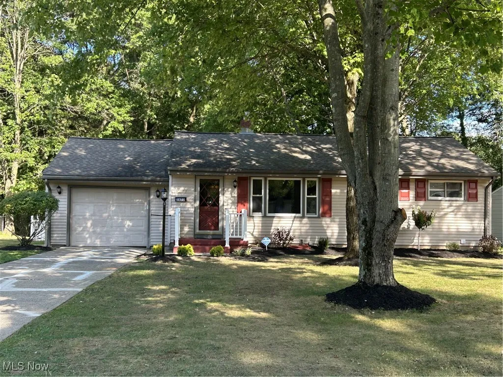 Ranch-style home with concrete driveway, an attached garage, a shingled roof, a front lawn, and a chimney
