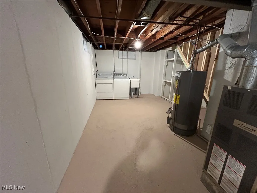 Unfinished below grade area with gas water heater, heating unit, and washer and clothes dryer